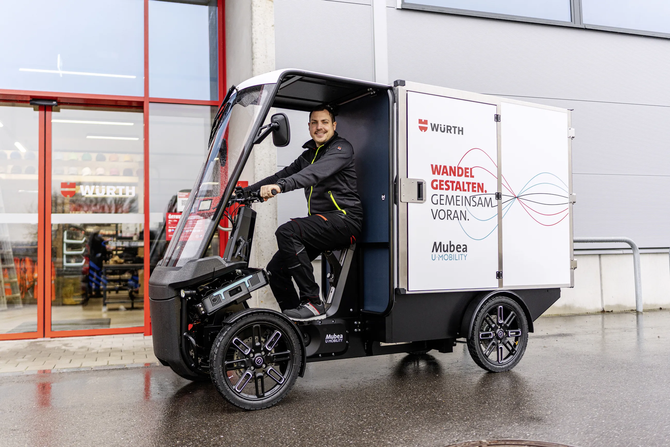 Junger Mann fährt Würth E-Cargobike vor moderner Fassade.