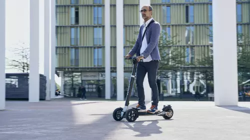 Ein Mann fährt in Freizeitkleidung auf einem XBoard in einer modernen städtischen Umgebung. Im Hintergrund sind hohe Gebäude und das Novotel-Logo zu sehen.