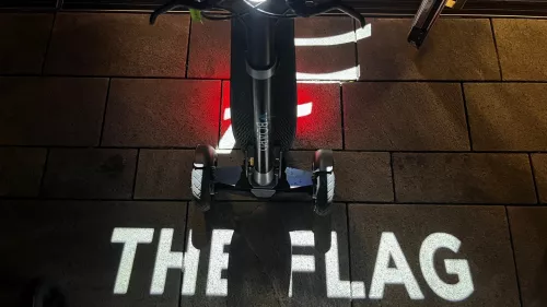 Ein XBoard steht im dunklen auf dem "The Flag" Logo, das in weißer Schrift auf dem Boden zu sehen ist. Außerdem sieht man das angeschaltete rote Rücklicht des XBoards.