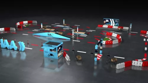 Das Bild zeigt einen Parcours, der auf der IAA Transportation Messe aufgebaut ist. Zu sehen ist ein klar markierter Streckenverlauf inklusive einer Rampe, der von rot-weißen Absperrungen und Schildern begleitet wird. Es sind verschiedene Elemente wie eine blaue IAA-Box und Werbetafeln zu sehen, die das Messeerlebnis unterstützen.
