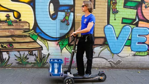 Digital X 2024: Fahrer transportiert einen Wasserkasten mit einem E-Scooter
