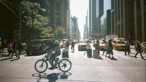 Frontal view of a street in New York, people crossing a zebra crossing, cyclists in the foreground.