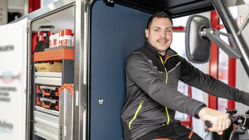 Junger Mann fährt mit einem E-Cargobike vor einem moderenem Gebäude.