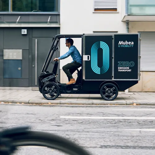 Cargo PACK drives onto the pavement in front of a modern residential building and delivers parcels.
